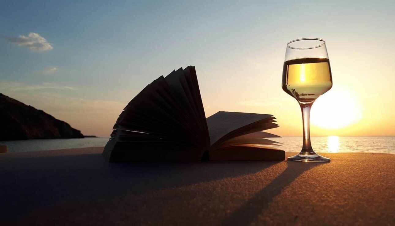 image of a glass of white wine with a book and sun setting in Lesvos, Greece